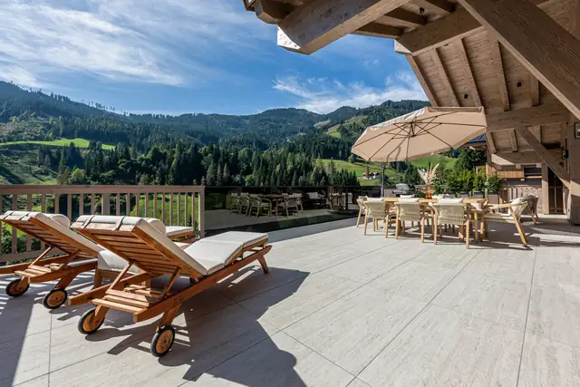 Terrasse mit Liegen und Esstisch, dahinter grüne Berge